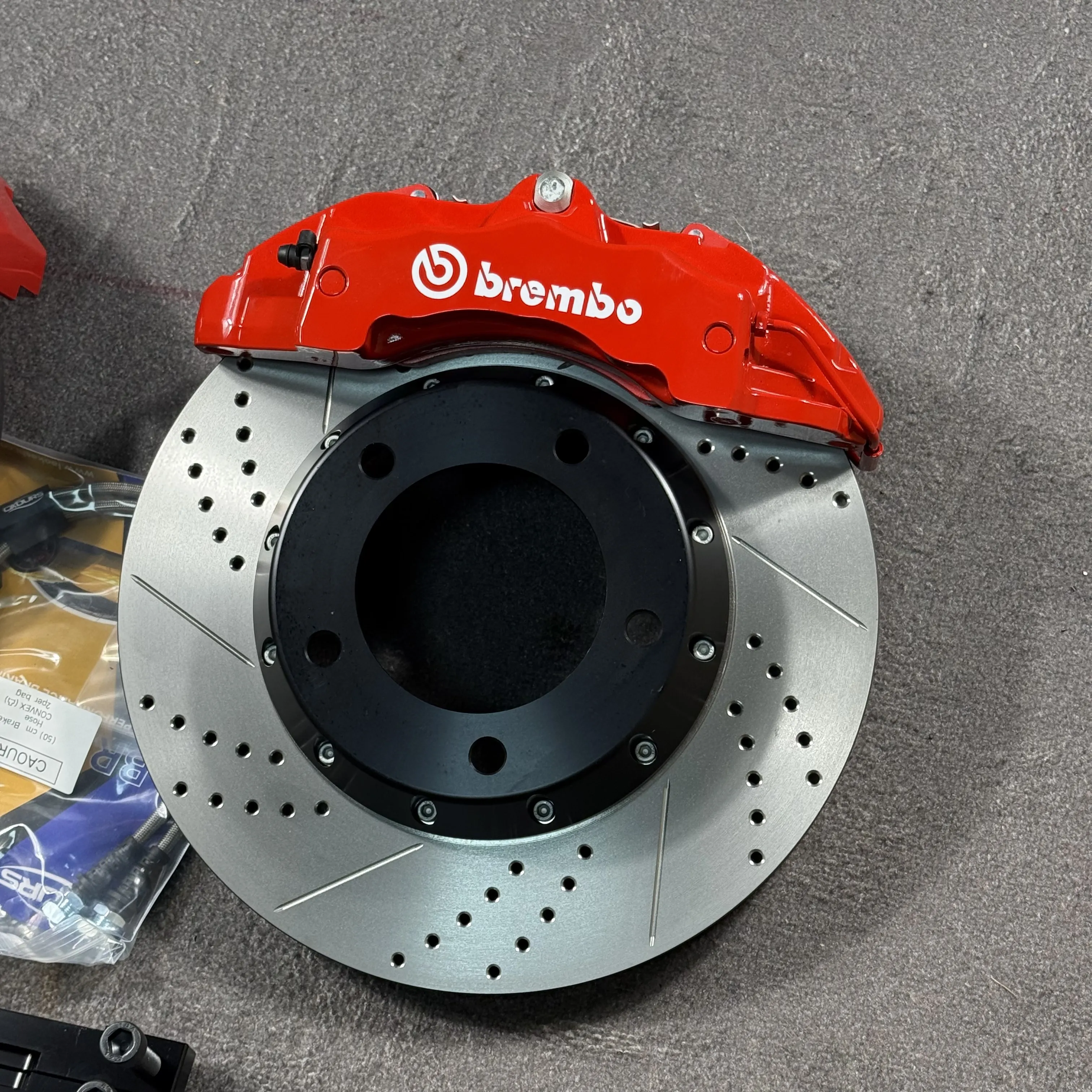 Шестипоршневой суппорт Brembo 18Z красного цвета на двухсоставном тормозном диске с перфорацией, насечками и чёрным алюминиевым колоколом