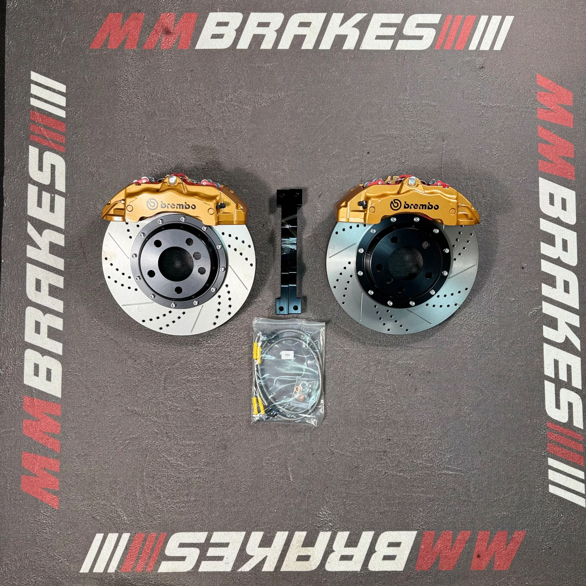 Золотистые шестипоршневые суппорты Brembo 18Z с перфорированными дисками с насечками, кронштейны и шланги на коврике MM Brakes