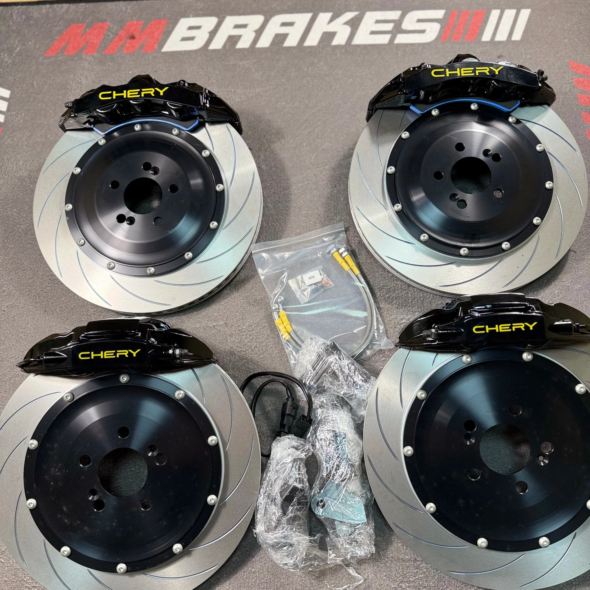 Комплект тормозов Brembo для Chery Tiggo: четыре чёрных суппорта с надписью CHERY, двухсоставные диски с насечками, шланги и датчики износа